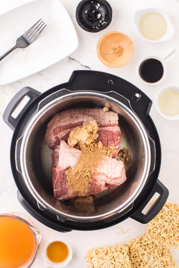 Pork shoulder in an Instant Pot with minced garlic and seasonings before cooking for Instant Pot Ramen