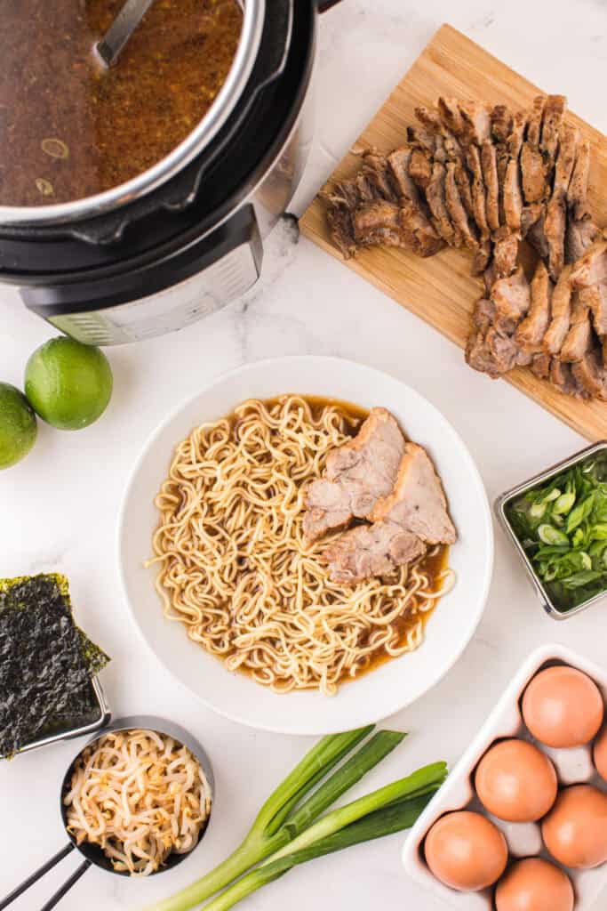 Bowl of Instant Pot Ramen with noodles and sliced pork beside an Instant Pot, sliced pork, green onions, bean sprouts, and nori