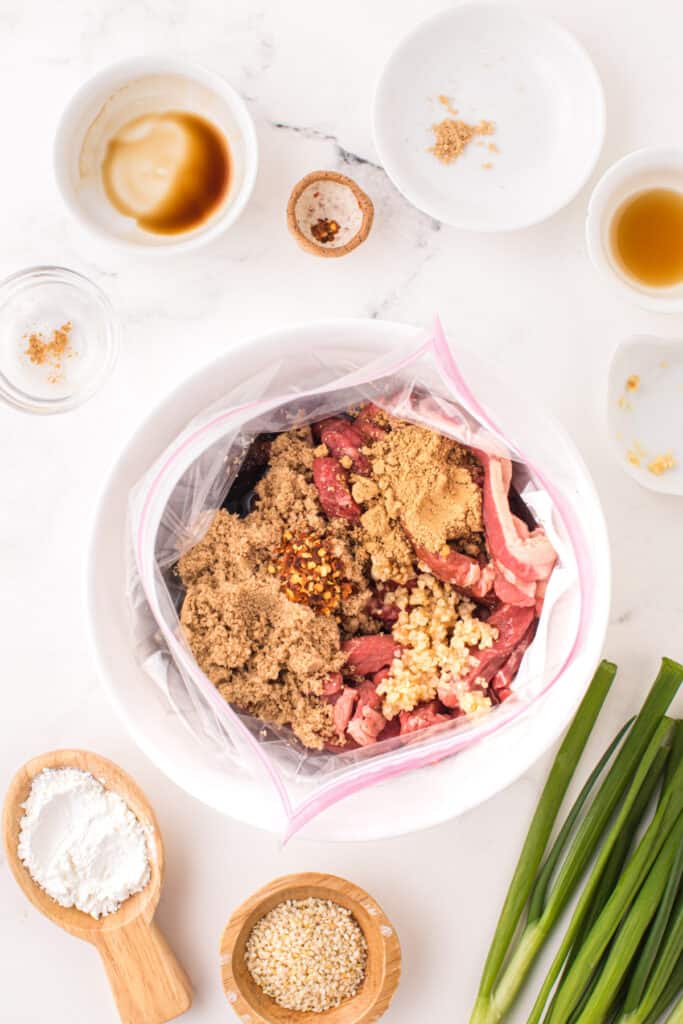 Ingredients for Korean Beef Bulgogi added to a sealable bag with sliced beef, garlic, brown sugar, soy sauce, and chili flakes