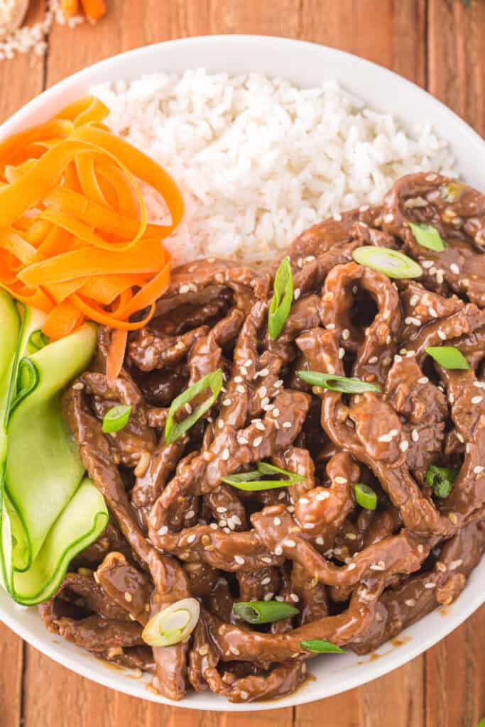 Korean Beef Bulgogi bowl served with white rice, carrot ribbons, cucumber ribbons, sesame seeds, and green onions