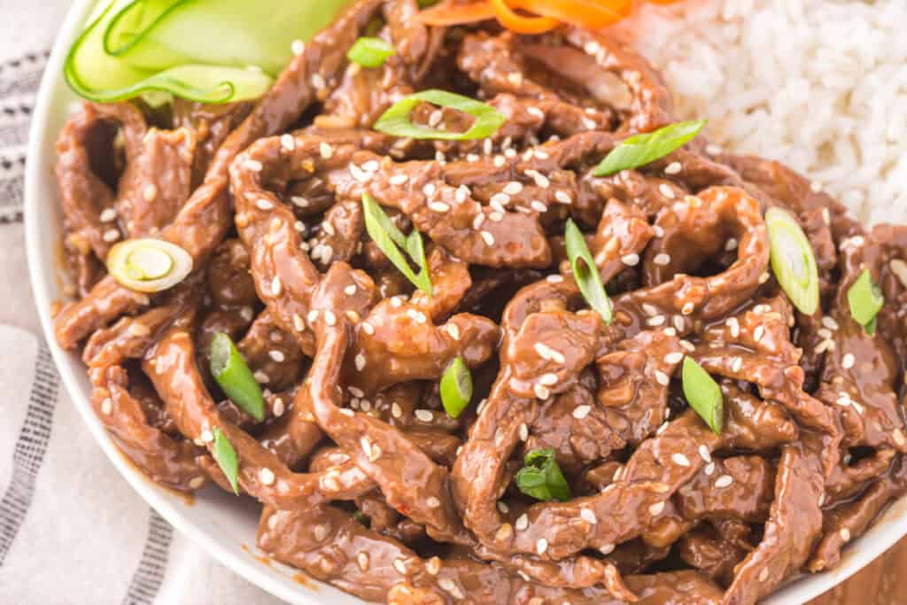 Korean Beef Bulgogi bowl with tender beef strips, white rice, cucumber ribbons, carrots, sesame seeds, and green onions