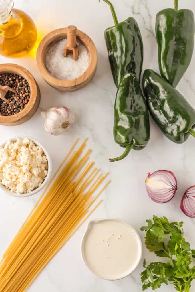 Ingredients for Mexican Green Spaghetti including poblano peppers, spaghetti, queso fresco, cream, garlic, and red onion