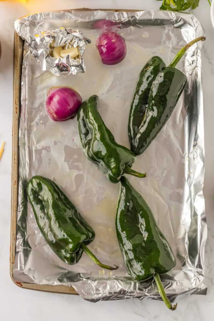 Poblano peppers, garlic, and red onion on baking sheet for Mexican Green Spaghetti recipe