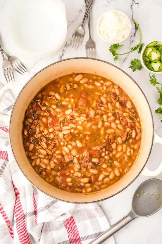 Finished Ranchero Beans in a Dutch oven with jalapeño slices, cilantro, and chopped onion for serving