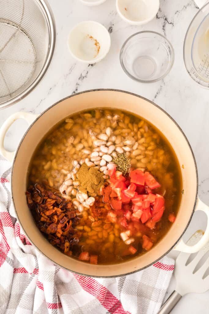 Ranchero Beans simmering in a Dutch oven with bacon and tomatoes