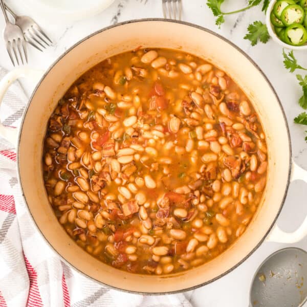 Ranchero Beans recipe in a Dutch oven with bacon, tomatoes, and pinto beans