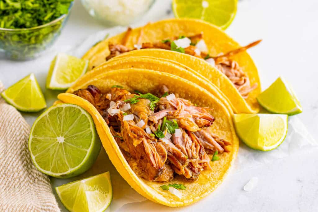 Slow Cooker Carnitas tacos with lime wedges, onion, and cilantro