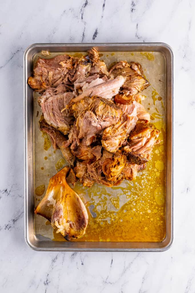 Cooked pork shoulder and bone on baking sheet for Slow Cooker Carnitas