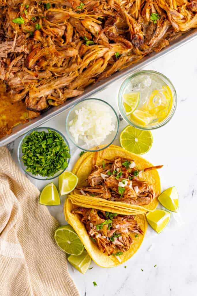 Slow Cooker Carnitas tacos with cilantro, onion, and lime wedges