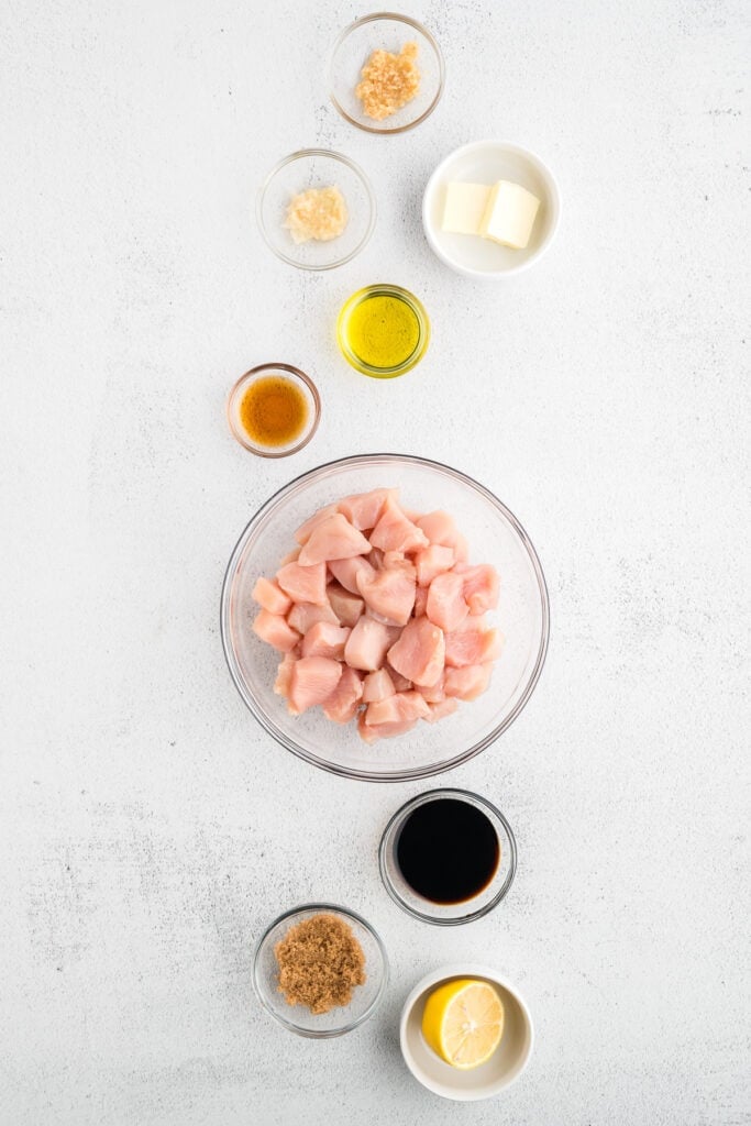 Overhead view of raw chicken breast pieces with soy sauce, sesame oil, garlic, ginger, brown sugar, butter, and lemon arranged for an easy Hibachi Chicken recipe.