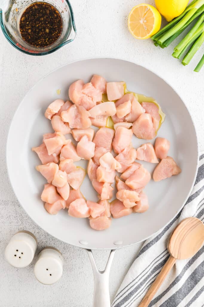 Raw chicken breast pieces cooking in a skillet for an easy Hibachi Chicken recipe with homemade hibachi sauce ingredients nearby.