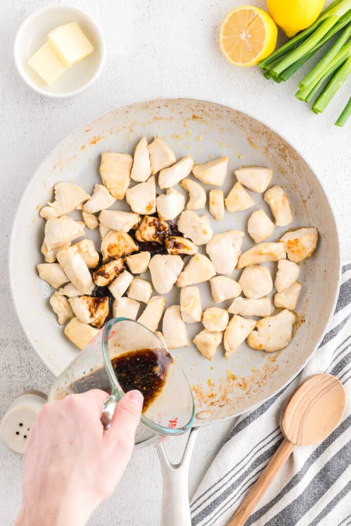 Pouring homemade hibachi sauce over cooked chicken pieces in a skillet for an easy Hibachi Chicken recipe.
