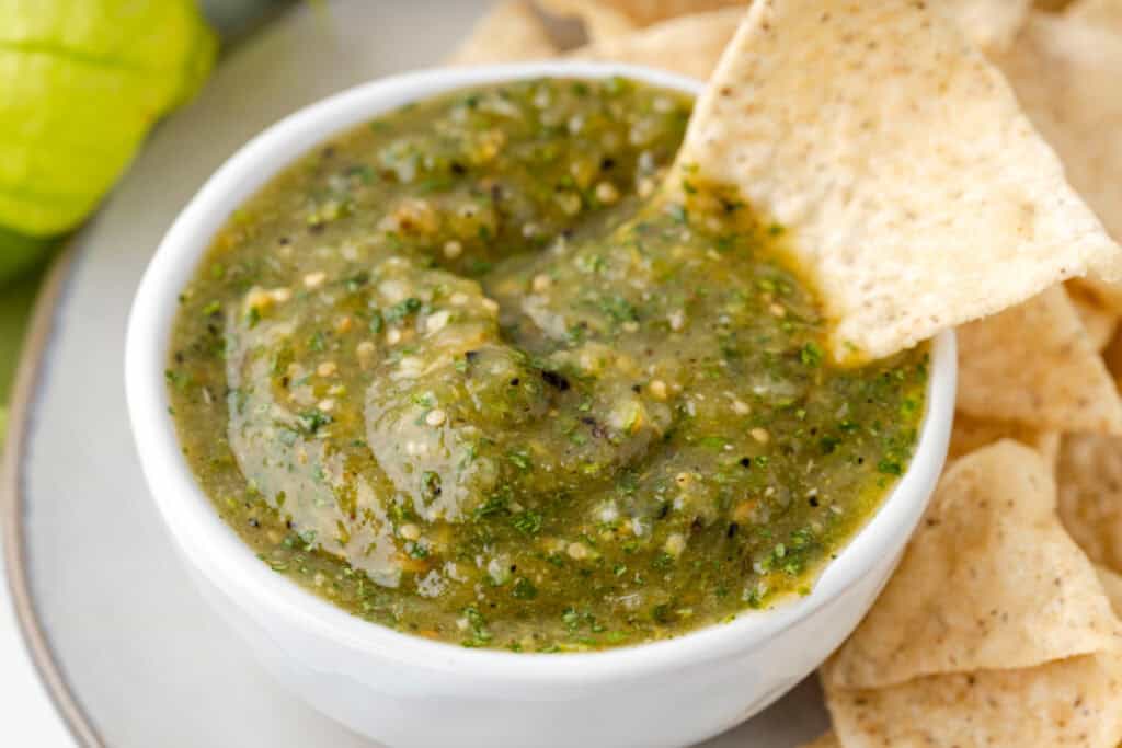 close-up of Tomatillo Salsa with visible herbs and seeds and a tortilla chip