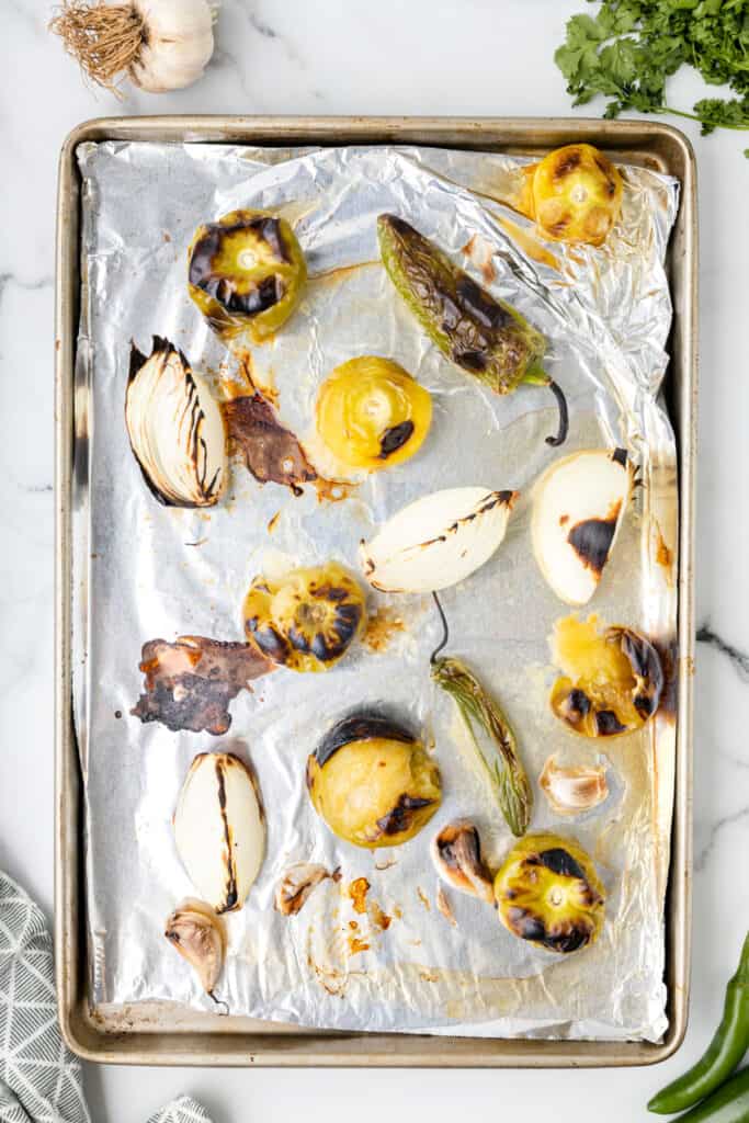 roasted tomatillos, charred onion, garlic, and peppers on a baking sheet for Tomatillo Salsa