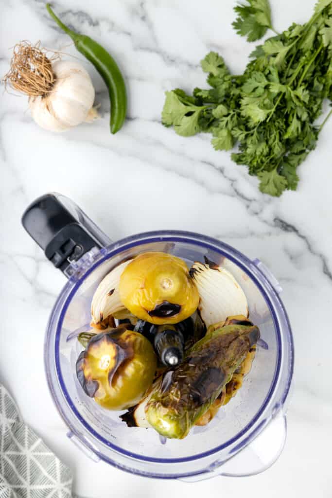 roasted tomatillos, onion, and peppers in a food processor ready to blend for Tomatillo Salsa