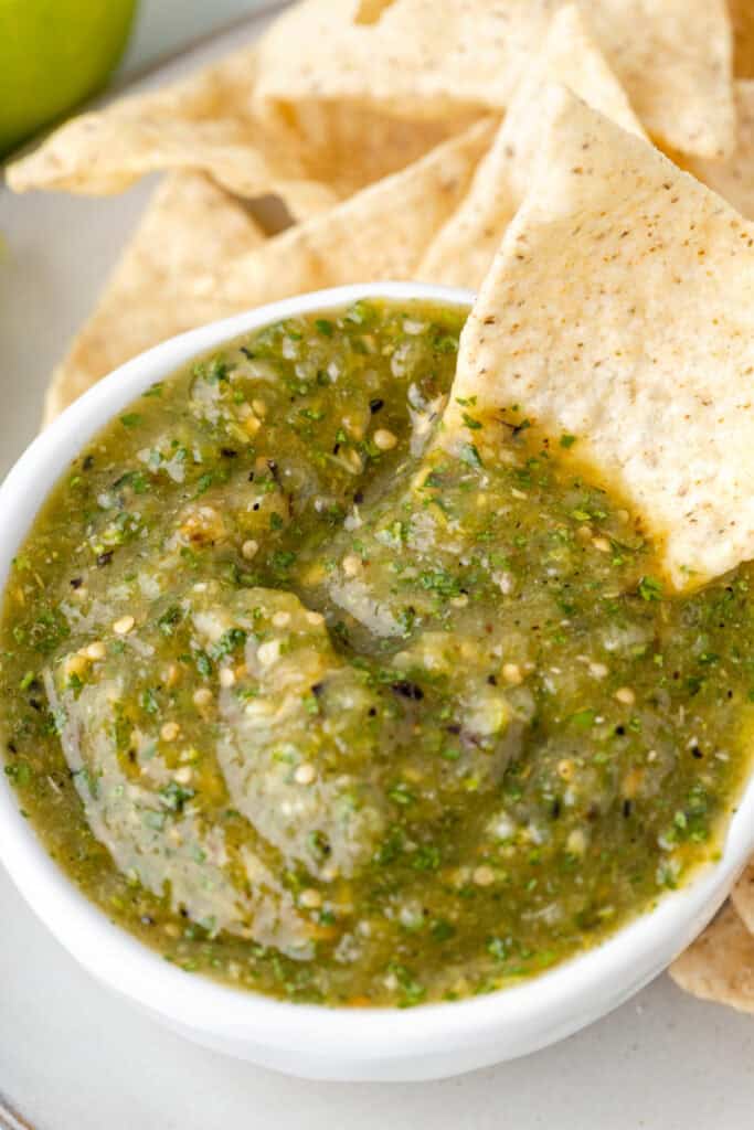 close-up of Tomatillo Salsa in a jar with tortilla chips in the background
