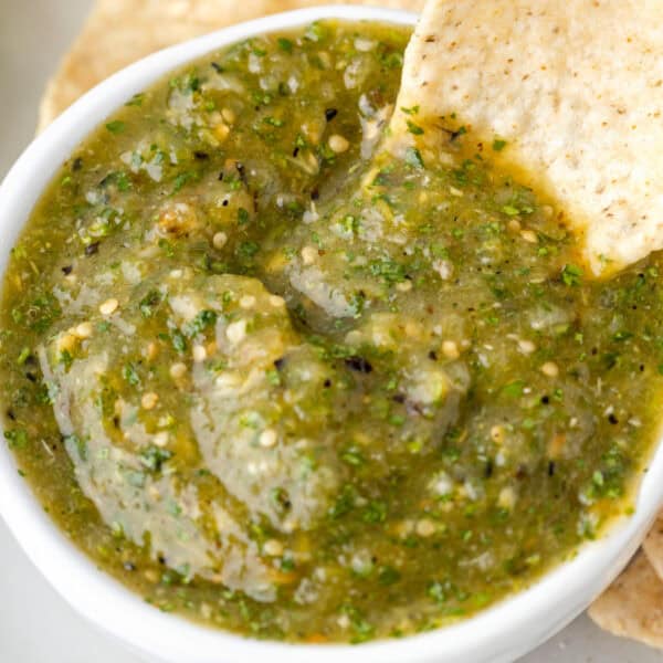 tortilla chip dipping into a bowl of Tomatillo Salsa with visible herbs, seeds, and slightly chunky texture