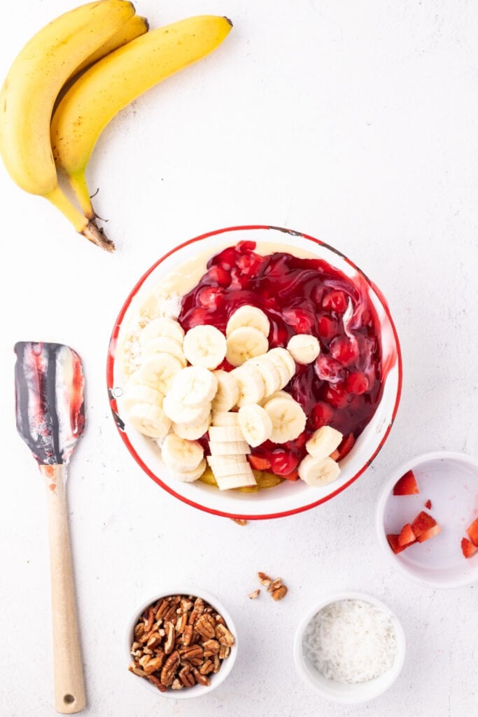 Sliced bananas added to a bowl of Banana Split Salad ingredients before mixing.