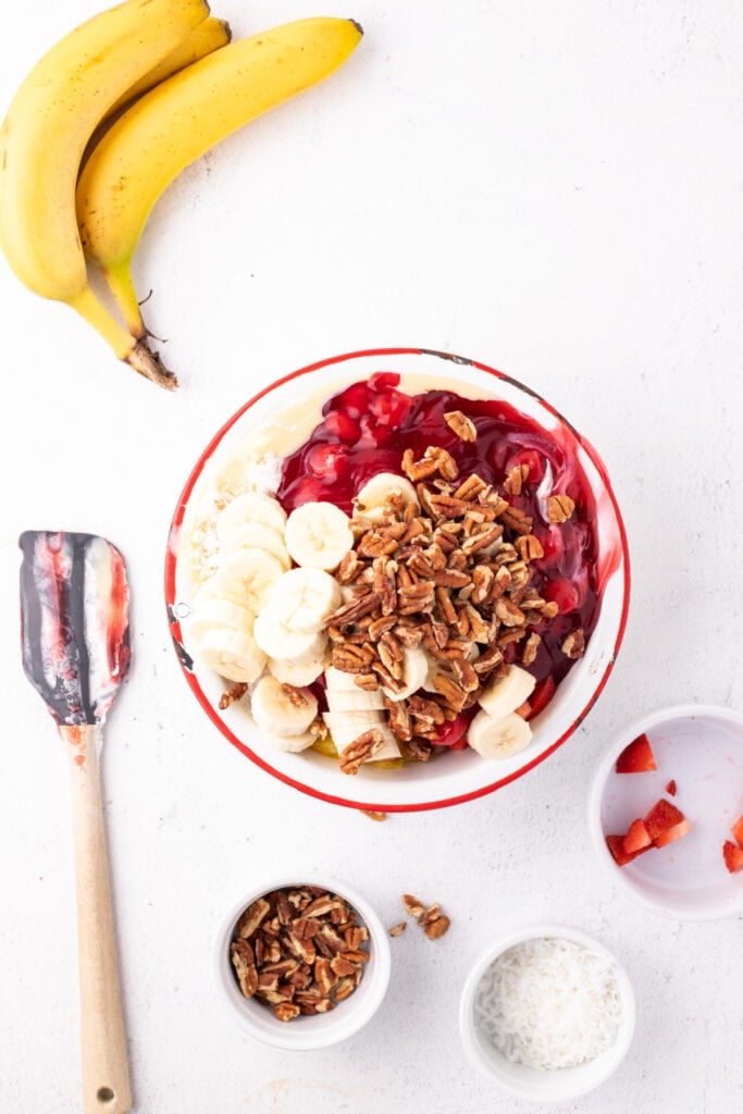 Chopped pecans added to a bowl of Banana Split Salad ingredients before stirring together.