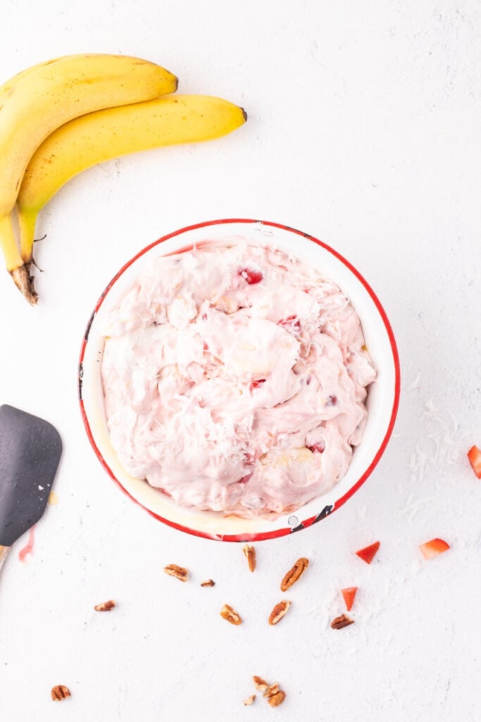 Mixed Banana Split Salad in a bowl with visible strawberries, bananas, coconut, and cherries in a creamy pink filling.