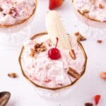 Banana Split Salad served in a glass dessert dish and topped with a banana half, maraschino cherry, coconut, and pecans, with additional dessert dishes in the background.