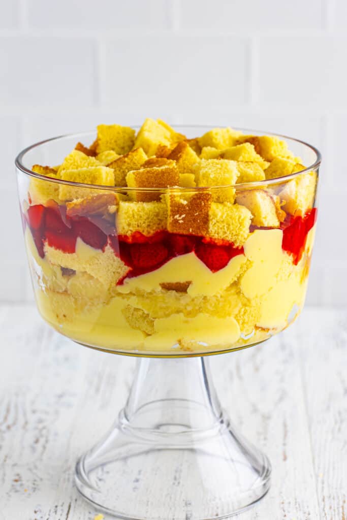Additional layer of cubed yellow cake added on top of strawberry pie filling in a clear trifle bowl for Banana Split Trifle.