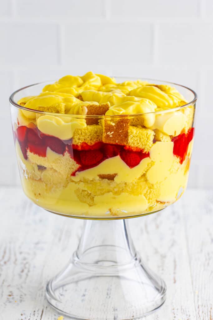Vanilla pudding spread over the top layer of cake cubes in a clear trifle bowl for Banana Split Trifle.
