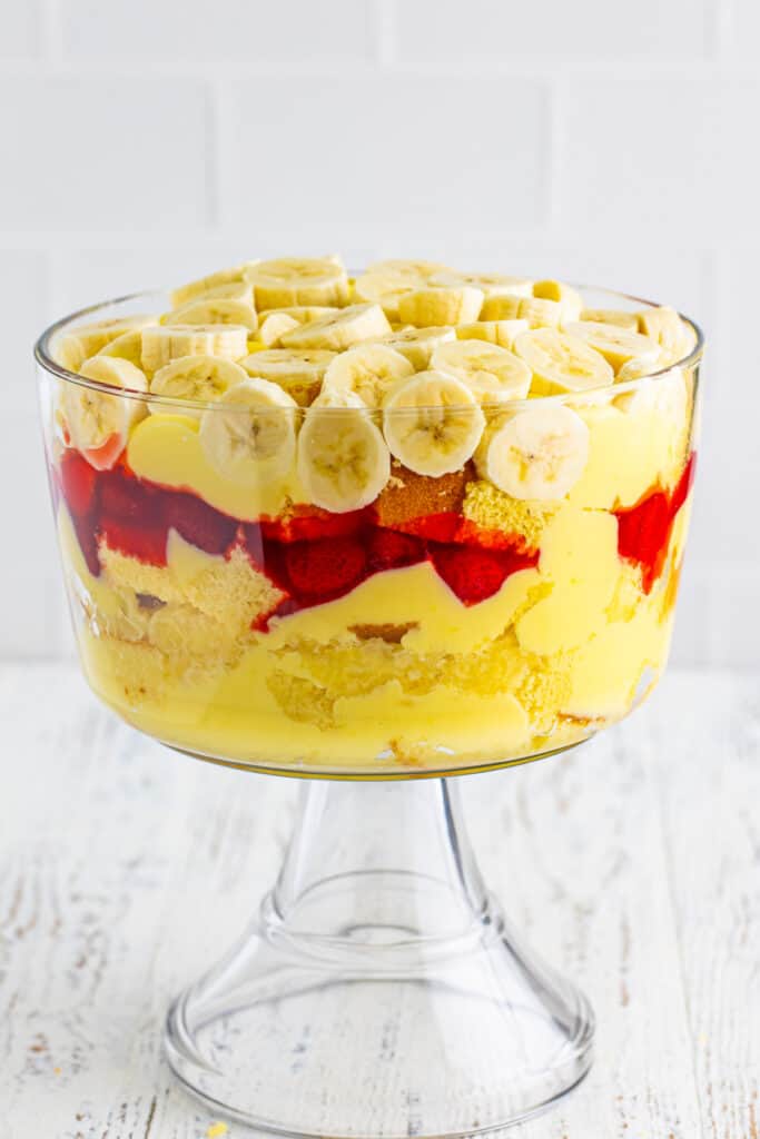 Sliced bananas arranged over the pudding layer in a clear trifle bowl for Banana Split Trifle.