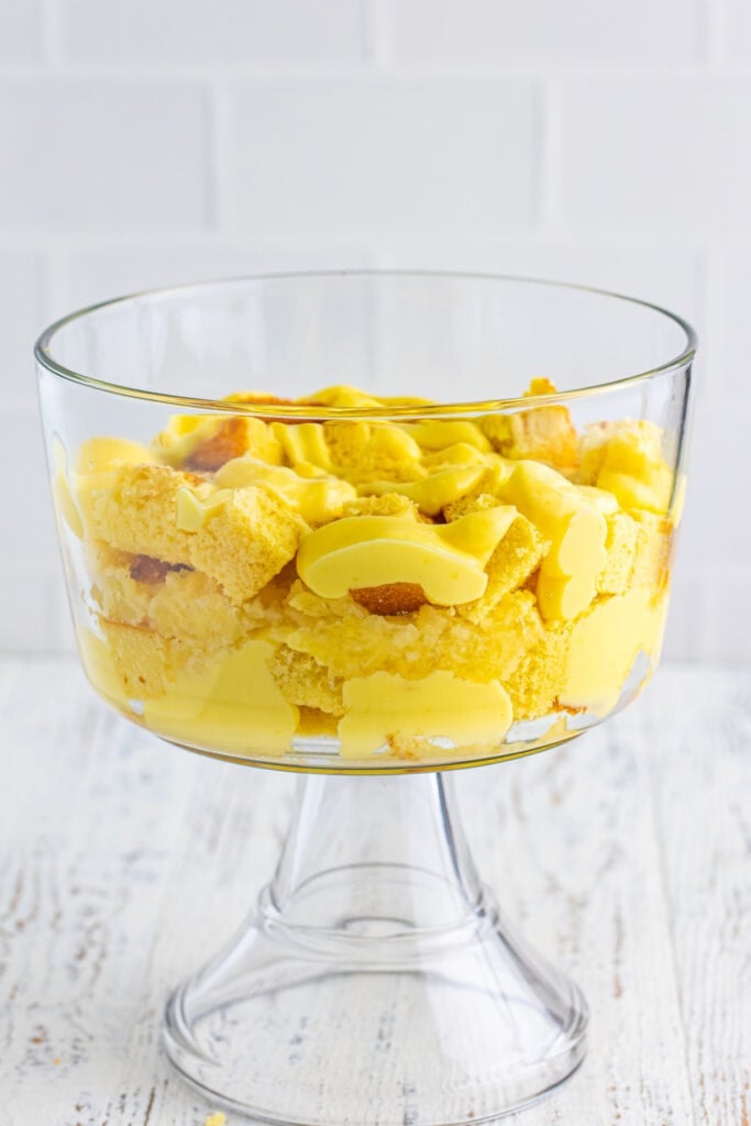 Second layer of vanilla pudding spooned over cake cubes in a clear trifle bowl for Banana Split Trifle.