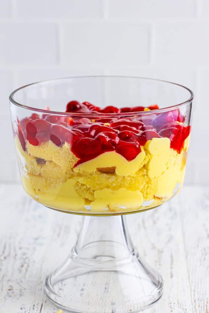 Layer of strawberry pie filling added to the trifle bowl over cake and pudding for Banana Split Trifle.