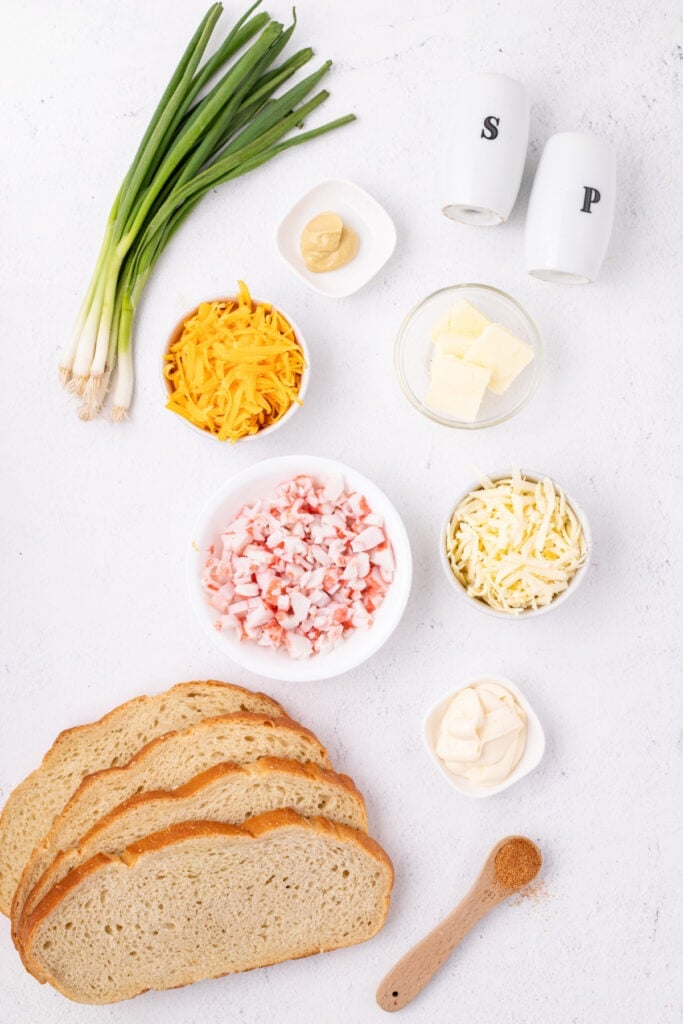 Ingredients for Cheesy Crab Melt including bread, imitation crab, shredded cheeses, mayonnaise, mustard, butter, green onions, and seasoning arranged on a countertop