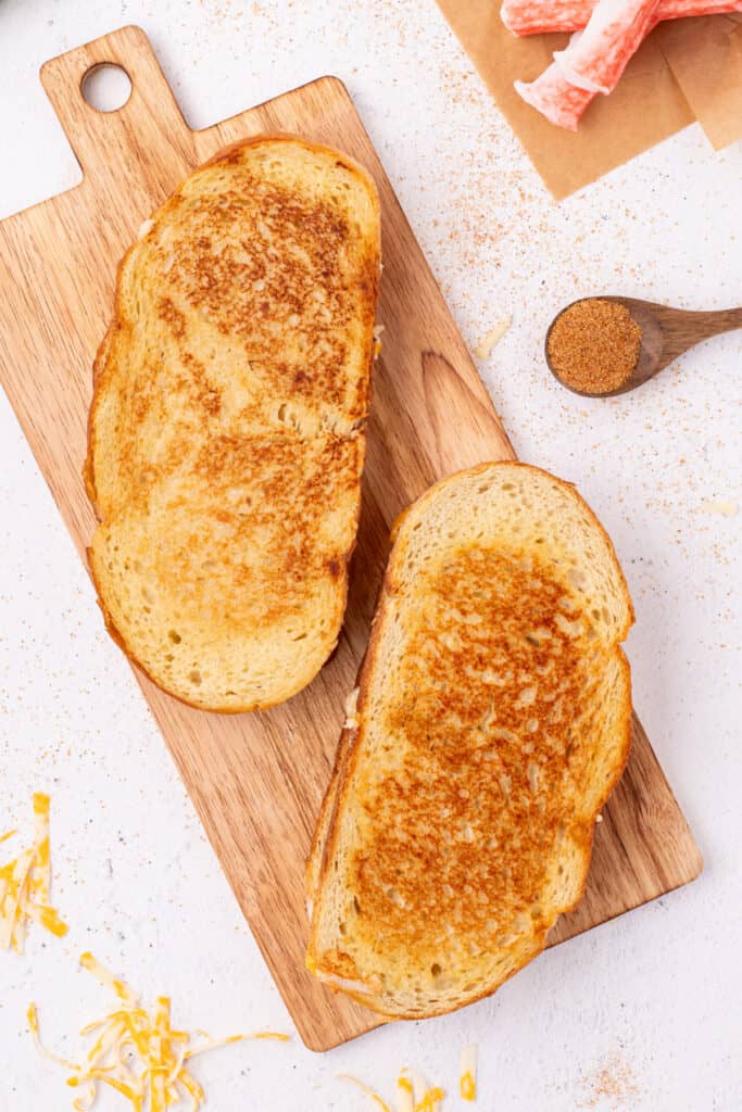 Two golden brown Cheesy Crab Melt sandwiches on a wooden cutting board