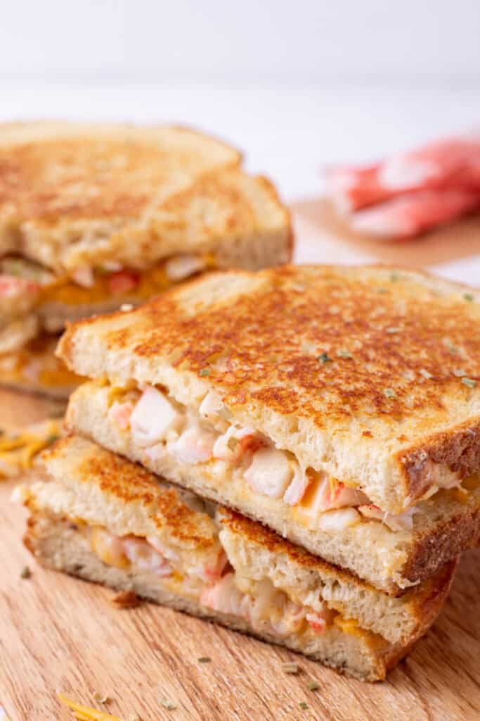 Stacked halves of Cheesy Crab Melt sandwiches on a wooden cutting board