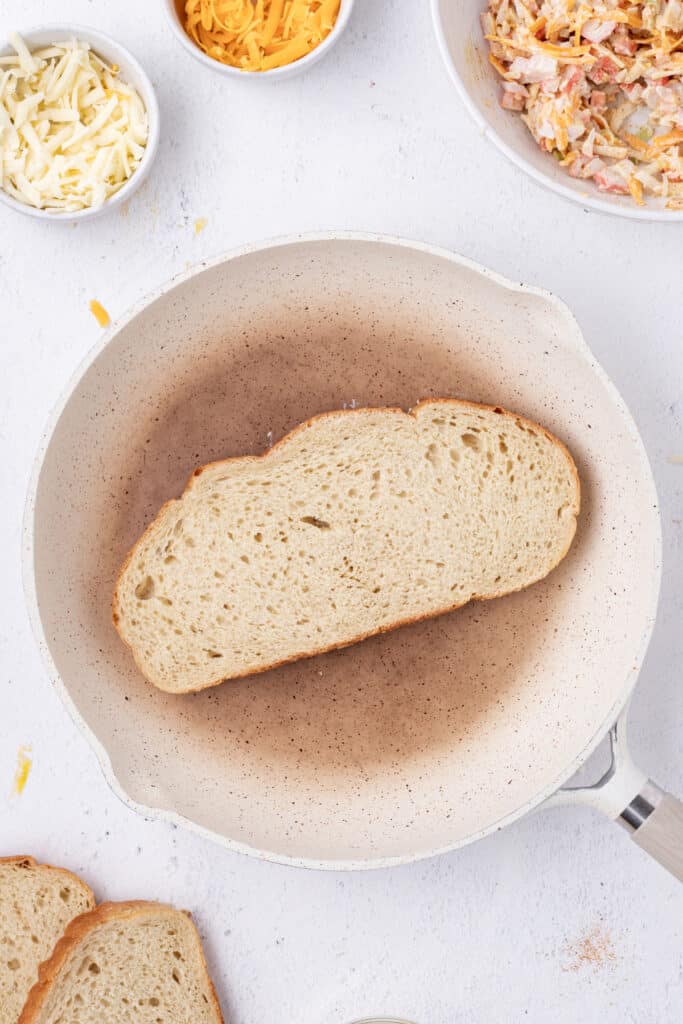 Slice of sourdough bread placed in a skillet for making a Cheesy Crab Melt