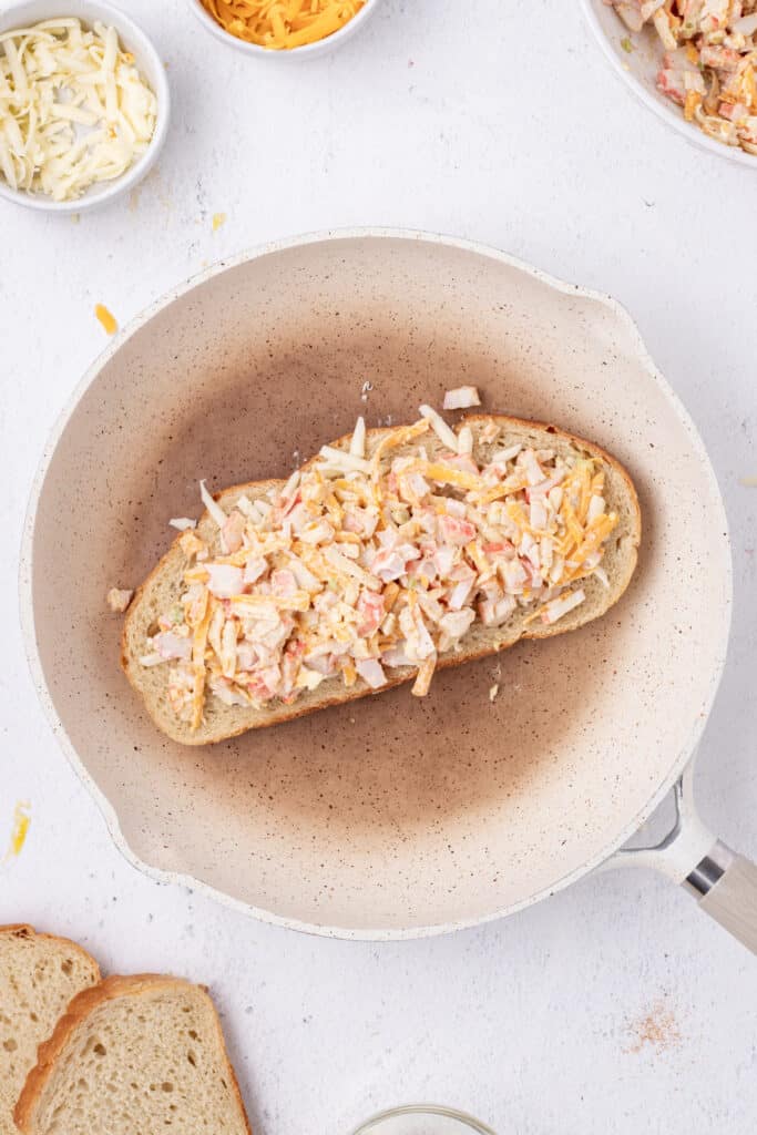 Cheesy crab filling spread over cheese on a slice of sourdough bread in a skillet