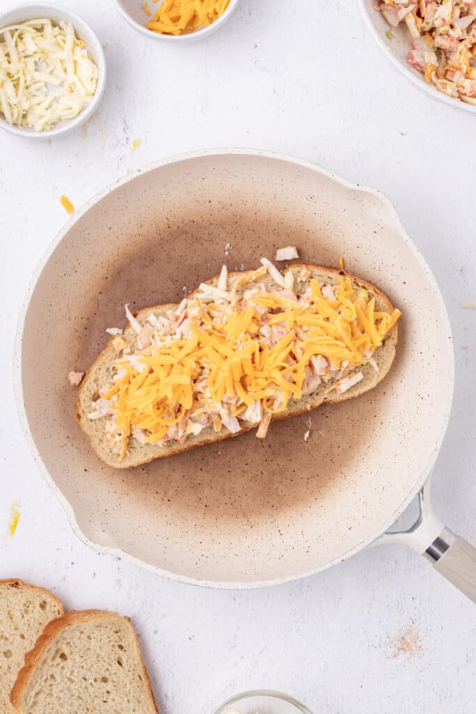 Shredded Cheddar cheese added on top of the crab filling in a skillet