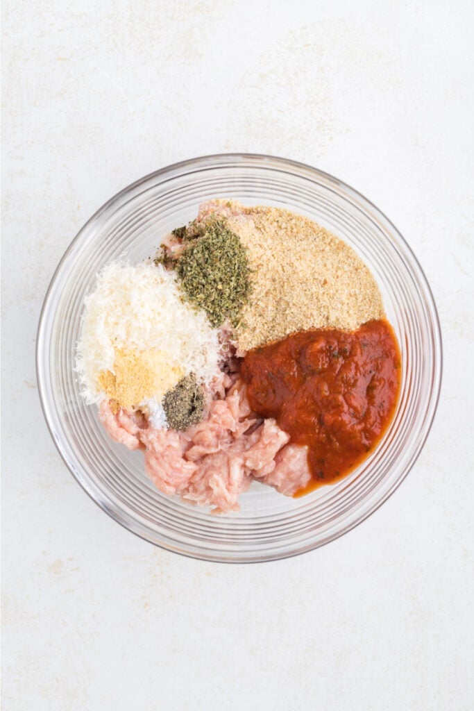 Ground chicken, marinara sauce, breadcrumbs, Parmesan cheese, and seasonings in a glass mixing bowl