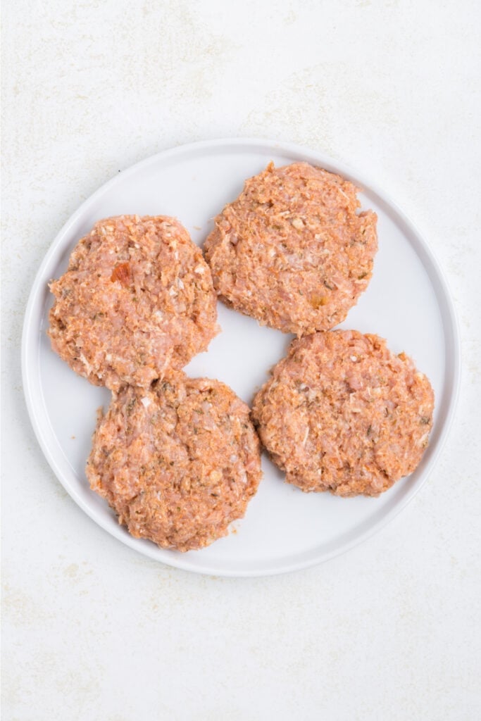 Four uncooked Chicken Parm Burger patties on a white plate
