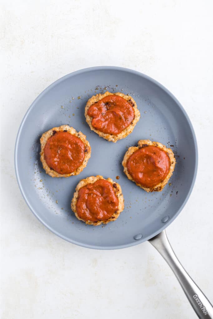 Cooked Chicken Parm Burger patties topped with marinara sauce in a skillet