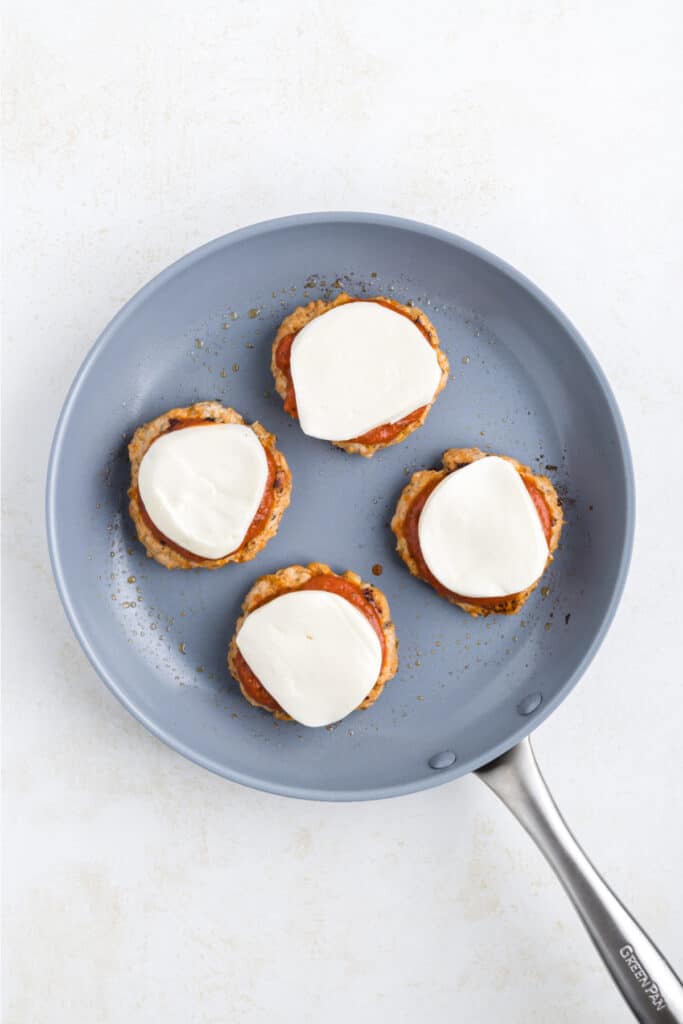 Chicken Parm Burger patties topped with marinara sauce and mozzarella cheese in a skillet