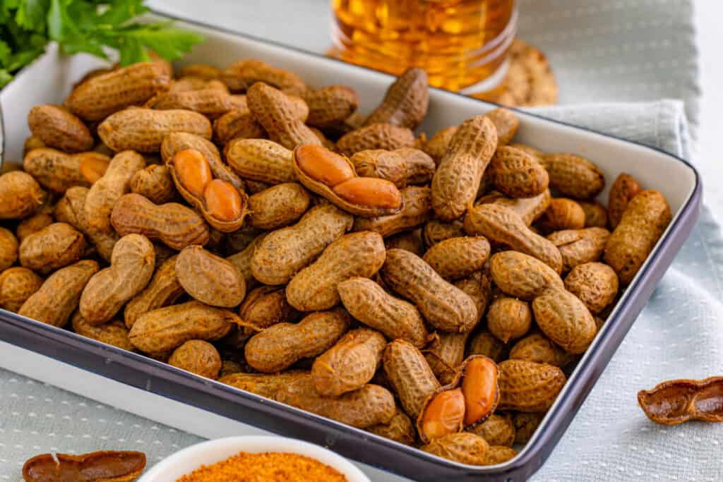 Serving dish filled with homemade Creole Boiled Peanuts, with a few peanuts opened to show the cooked peanuts inside.