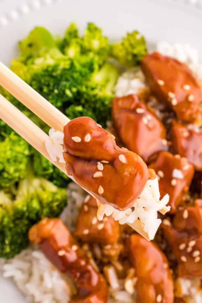 Chopsticks holding a bite of Mongolian Pork with rice and broccoli