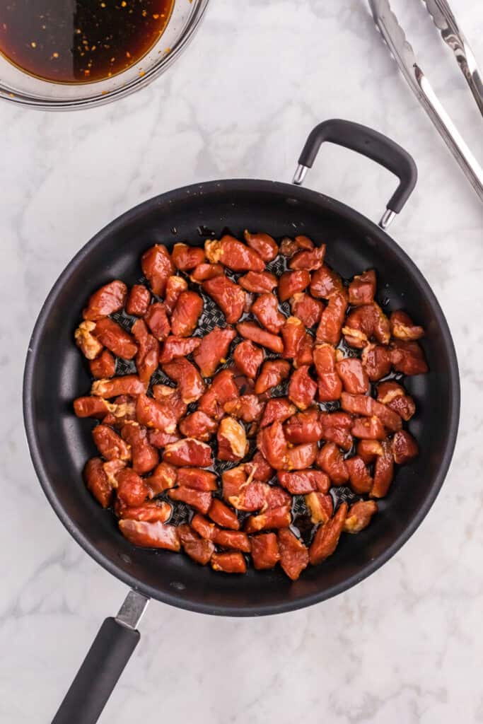 Marinated pork cooking in a skillet until browned