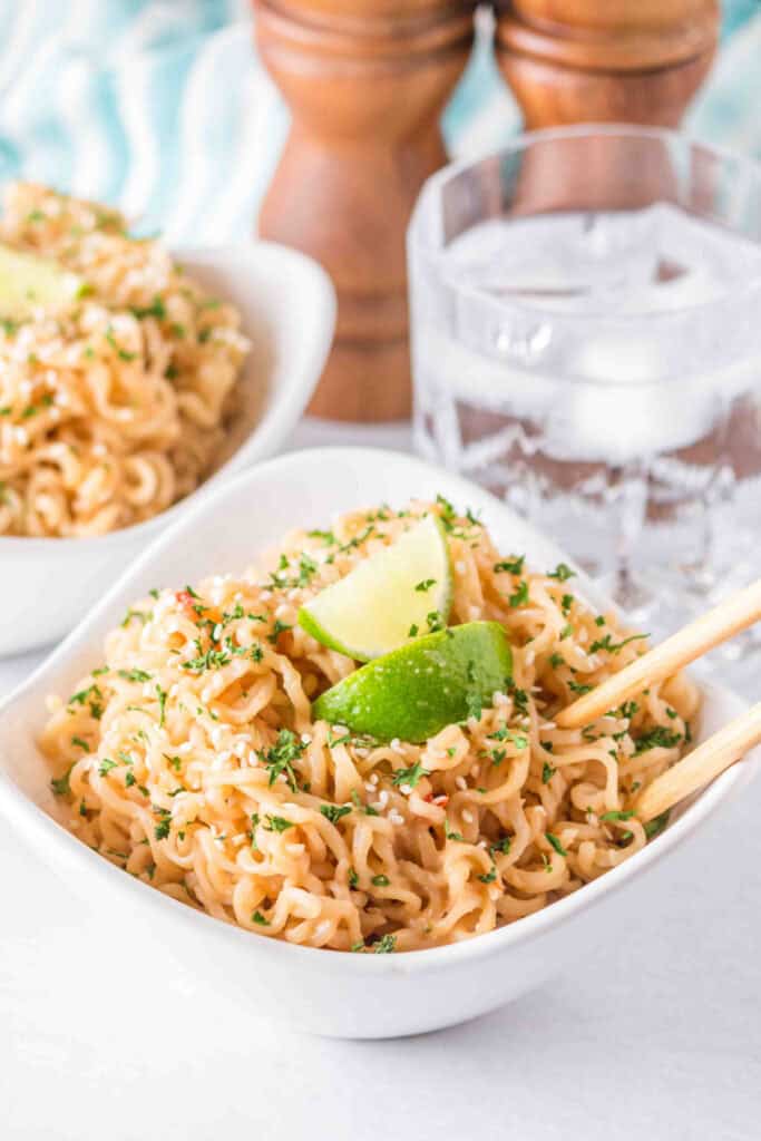 Bowl of creamy Peanut Butter Ramen Noodles garnished with sesame seeds, parsley, and lime wedges.