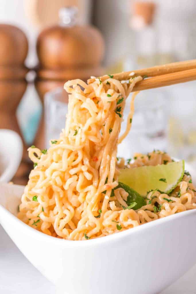 Close-up of creamy Peanut Butter Ramen Noodles topped with sesame seeds, parsley, and a fresh lime wedge.