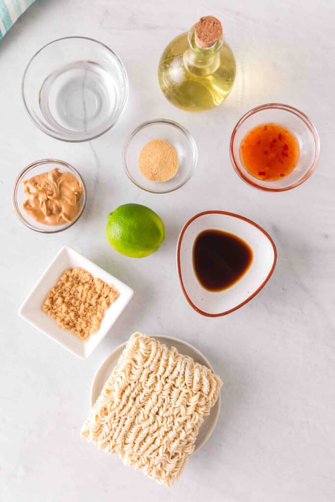 Ingredients for Peanut Butter Ramen Noodles including ramen noodles, peanut butter, lime, sriracha, Worcestershire sauce, brown sugar, garlic powder, olive oil, and water.