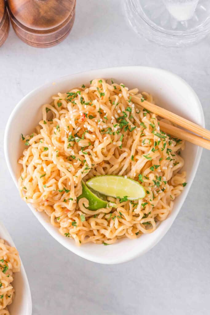 Overhead view of creamy Peanut Butter Ramen Noodles garnished with sesame seeds, parsley, and fresh lime.