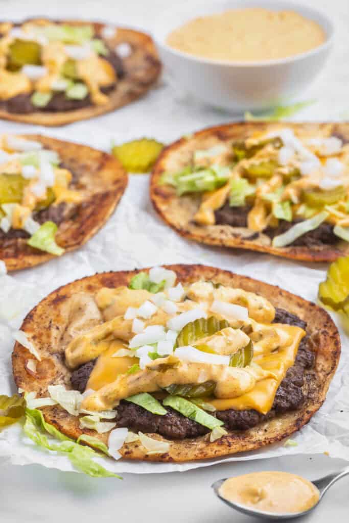 Smash Burger Tacos topped with cheese, burger sauce, lettuce, onions, and pickles served on parchment paper.