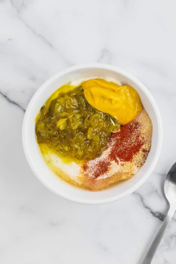 Mayonnaise, pickle relish, mustard, vinegar, paprika, onion powder, and garlic powder combined in a bowl before mixing.