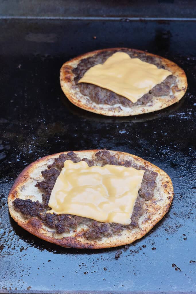 Smash Burger Tacos on a griddle topped with melted American cheese.